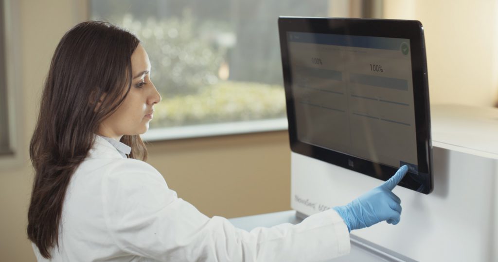 Woman in lab coat touching a computer screen.