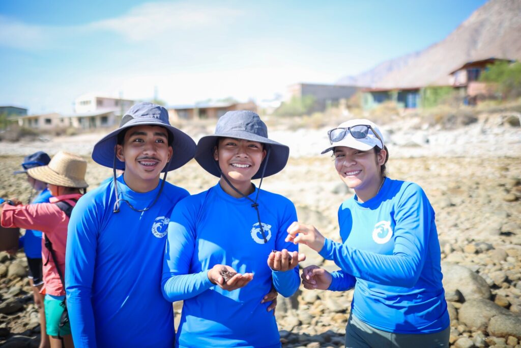 Three people in hats and blue ODI shirts smiling and holding sea creatures