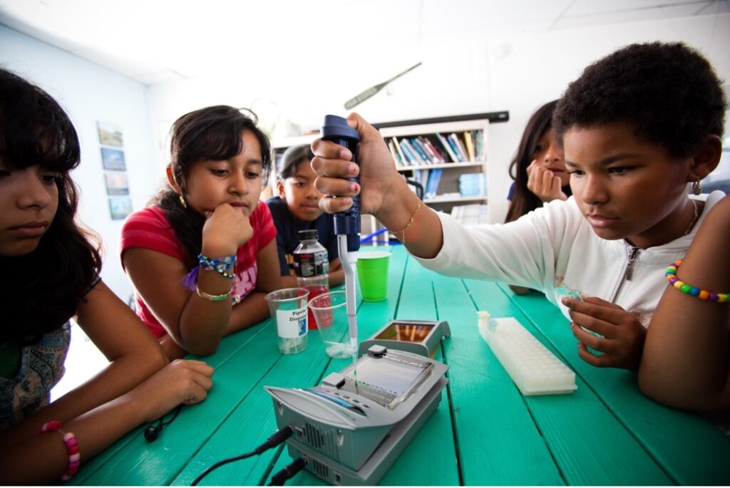 A group of students sit at a table and perform a science experiment.