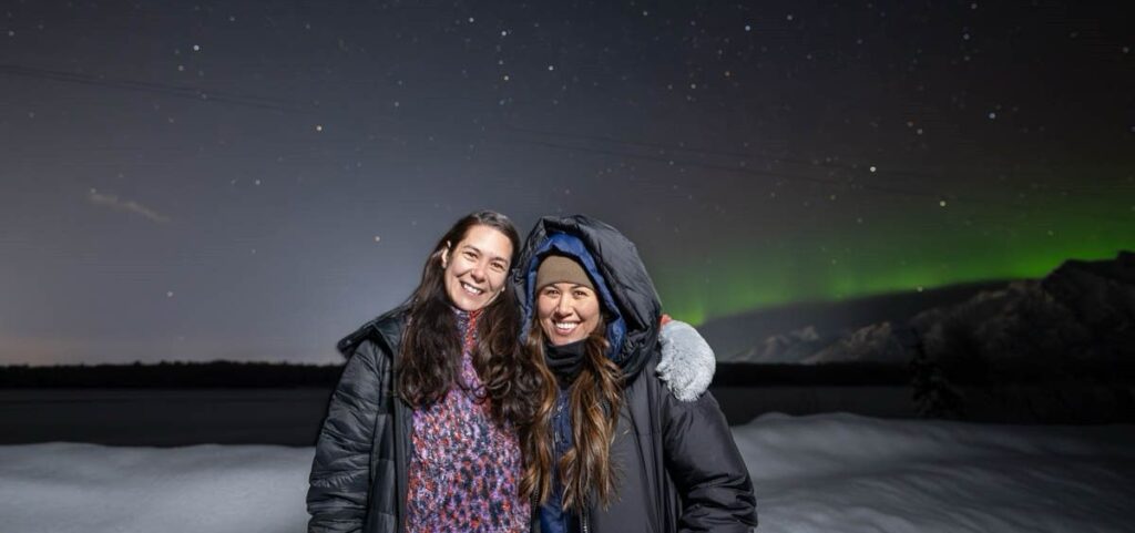 Two women pose together outside in front of a snowy background.